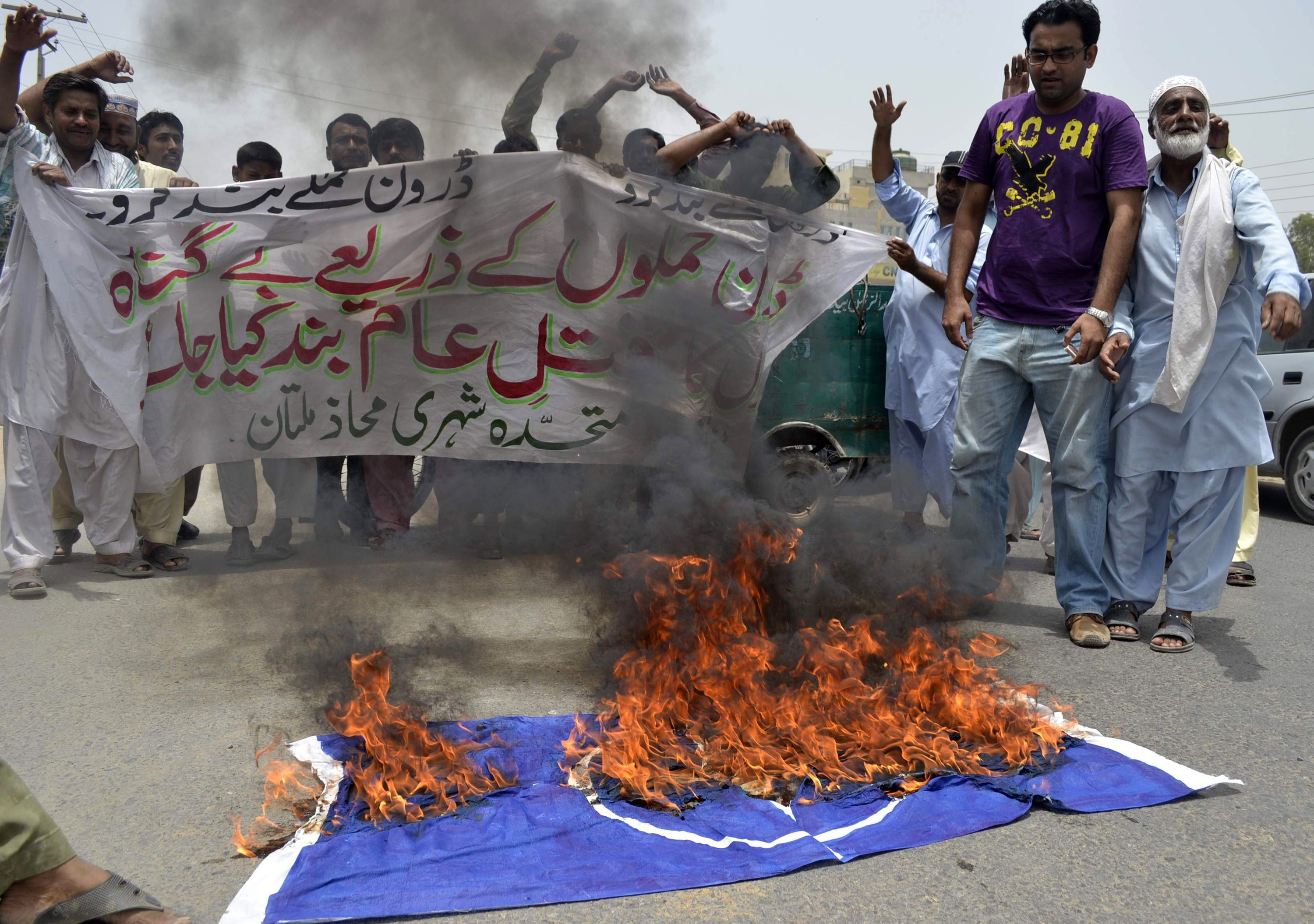Pakistani protesters shout slogans beside a burning NATO flag during a demonstration against drone attacks in Multan on June 27, 2012.