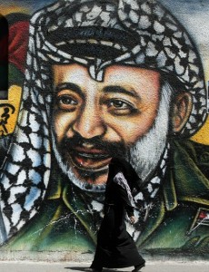 A Palestinian woman walks past a mural of late Palestinian leader Yasser Arafat in Gaza City AFP PHOTO/MAHMUD HAMS
