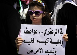 A young girl holds a sign in Arabic that reads  "In Zaatari, sand storms destroy tents and cause diseases" during a protest near UN offices in Amman demanding better living conditions at the Zaatari Syrian refugee camp AFP PHOTO/KHALIL MAZRAAWI 