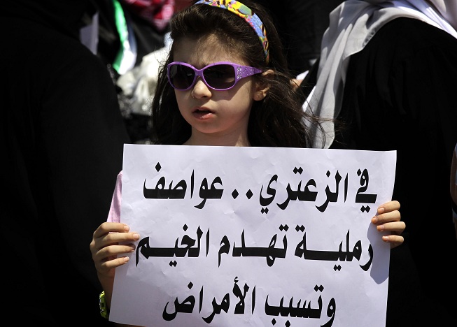 A young girl holds a sign in Arabic that reads "In Zaatari, sand storms destroy tents and cause diseases" during a protest near UN offices in Amman demanding better living conditions at the Zaatari Syrian refugee camp AFP PHOTO/KHALIL MAZRAAWI