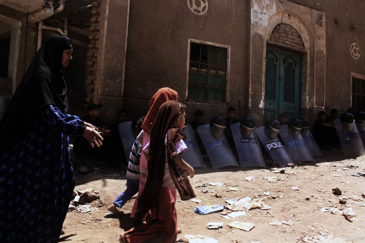 Egyptian riot policemen sit in the shade by damaged buildings on August 2, 2012, as an Egyptian woman and children walk through debris from the aftermath of clashes on August 1, between Christians and Muslims in Dahshur village, on the outskirts of Cairo (file photo: AFP /TAREK EL GABBAS)