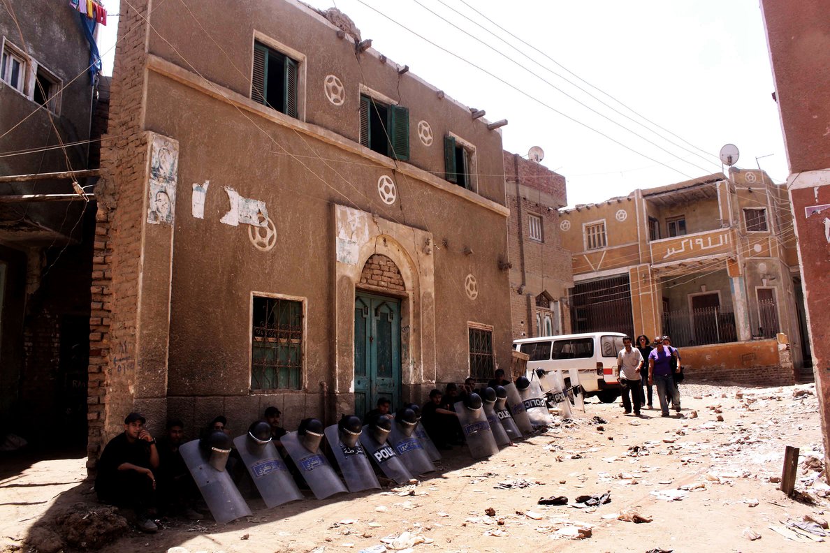 Egyptian riot policemen sit in the shade by damaged buildings on 2 August as people walk through debris from the aftermath of clashes on 1 August between Christians and Muslims in Dahshur village, on the outskirts of Cairo AFP PHOTO/TAREK EL GABBAS