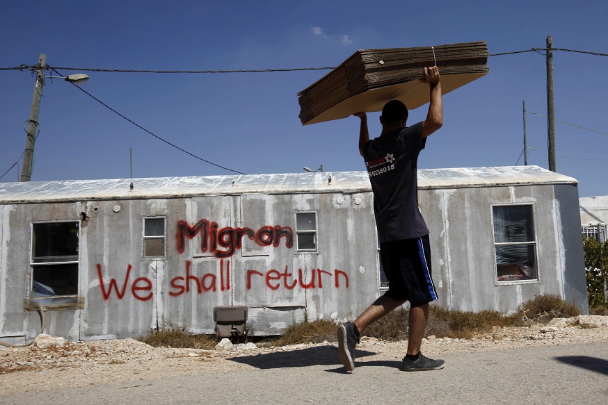 An Israeli moving company employee carries cardboard for boxes as he walks past a caravan of evacuated settlers in the Migron outpost in the occupied West Bank on 2 September AFP PHOTO / GALI TIBBON
