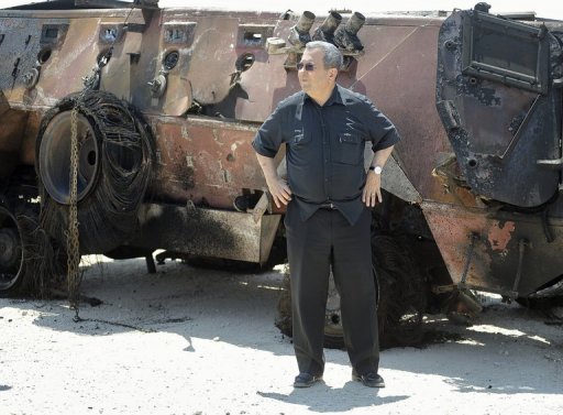 Israeli Defence Minister Ehud stand next to a burnt armoured vehicle near the Karam Salem border crossing on August 6, 2012