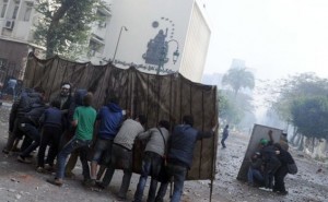 Protesters against the Prime Minister and his cabinet use makeshift shields to approach the Shura Council building during clashes with the army in December 2011 (photo: AFP/Mohamed Hossam)