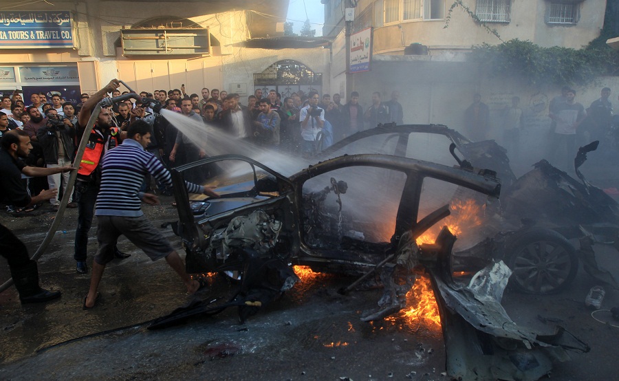 Palestinians extinguish fire from the car of Ahmaed Jaabari, head of the military wing of the Hamas movement, the Ezzedin Qassam Brigades, after it was hit by an Israeli air strike in Gaza City (Photo by AFP / Mahmud Hams)