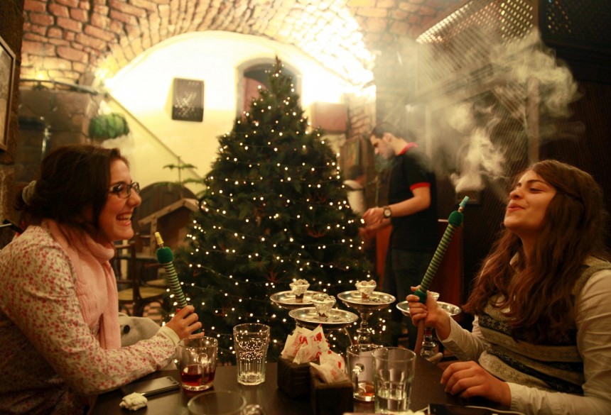 Syrian women smoke shisha as a waiter decorates the Christmas tree at a cafe in the old city of Damascus. The majority of the Christian community in Syria has decided to celebrate Christmas without decorations this year amid the ongoing Syrian conflict but the owner of the cafe decided to carry on with the tradition regardless. AFP Photo / Carole Alfarah