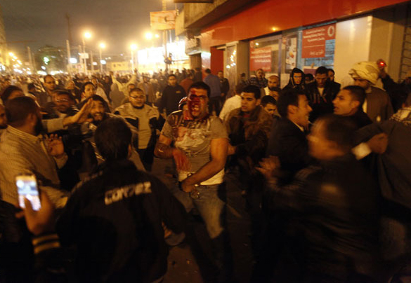 An injured Egyptian opposition protester (centre) runs as he is surrounded by members of the Muslim Brotherhood and supporters of President Morsy during clashes with anti-Morsy demonstrators on the road leading to the Egyptian presidential palace on 5 December (AFP Photo / Mahmoud Khaled)