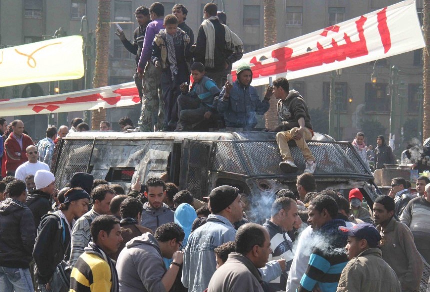 Bystanders gather around a burnt out police van in Tahrir Square on 29 January Mohamed Omar
