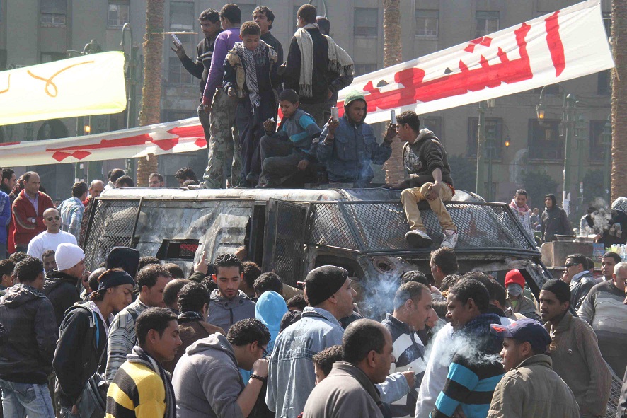 Bystanders gather around a burnt out police van in Tahrir Square on 29 January Mohamed Omar