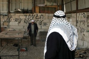 A Palestinian man walks past a wall sprayed with graffiti written in Hebrew in the village of Beit Ummar, north of the West Bank city of Hebron, on 1 January 2013. (AFP PHOTO)