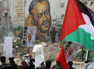 Palestinians raise up flags and placards a rally commemorating the 37th anniversary of "Land Day", in front of the Israeli separation barrier covered with grafittis (AFP Photo)