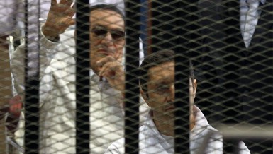 Alaa Mubarak, son of ousted Egyptian president Hosni Mubarak, (back) sits in front of his father behind bars during a hearing in their retrial at the Police Academy in Cairo  (AFP Photo)