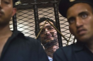 Egyptian political activist Ahmed Douma smiles as he stands behind dock bars during his trial in Cairo on May 13, 2013 on charges of insulting president Mohamed Morsi in a TV interview. (AFP Photo\ Khaled Desouki)